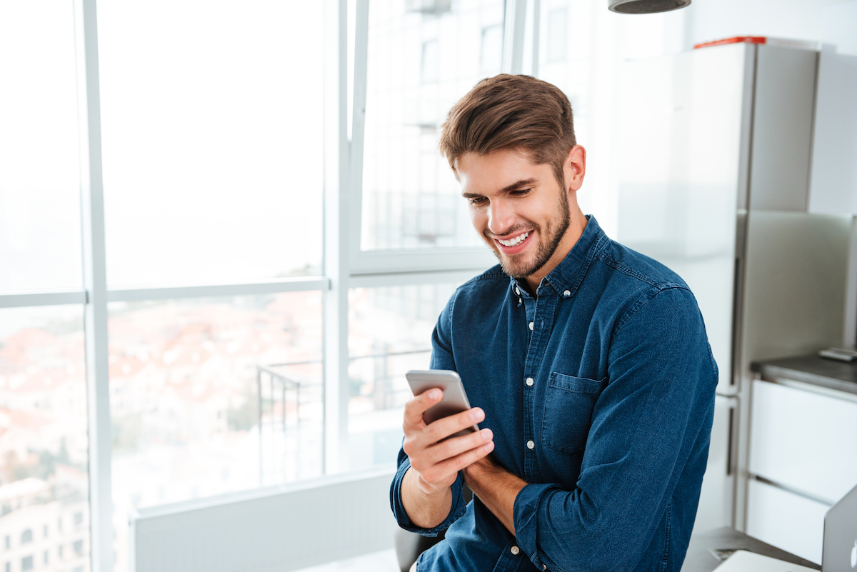 Picture of young man using a smartphone and smiling. Looking at smartphone.