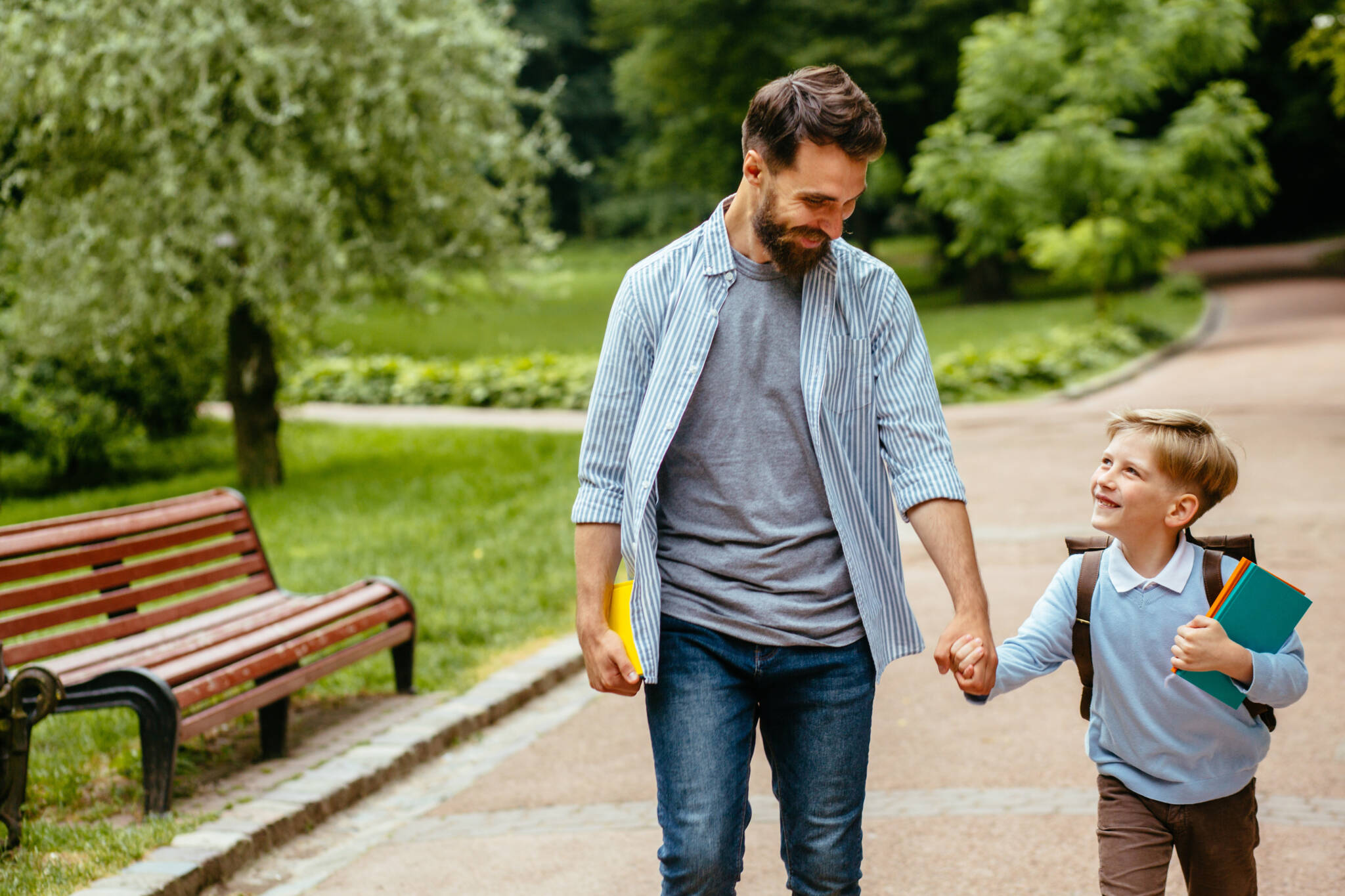 Parent take child to school. Pupil of primary school go study with backpack outdoors. Father and son go hand in hand. Beginning of lessons. Back to school. First day of fall. Elementary student.