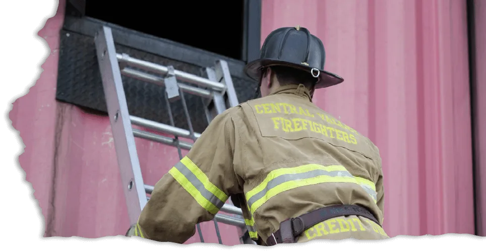 A firefighter in protective gear climbs a ladder towards a window on a pink building. "Central Valley Firefighters Credit Union" text is visible on the back of his uniform.