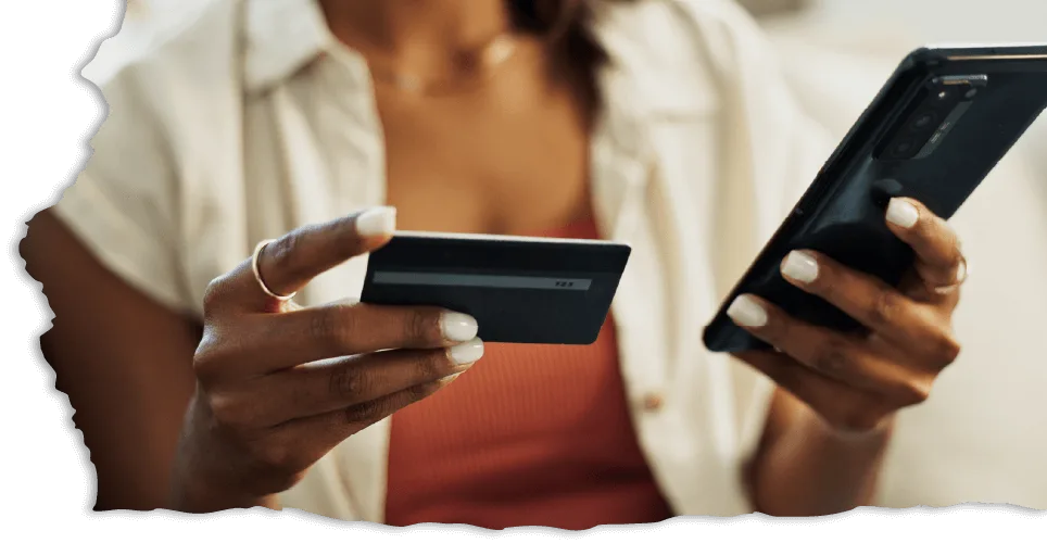 A person holds a credit card and smartphone, poised to make an online purchase.