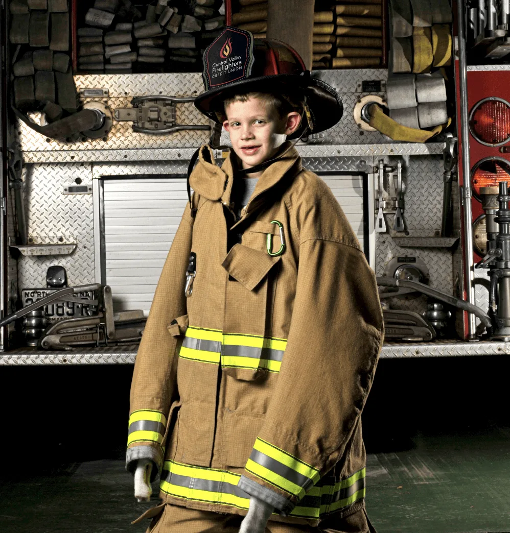 Young boy dressed up in oversized fireman's suit and hat.